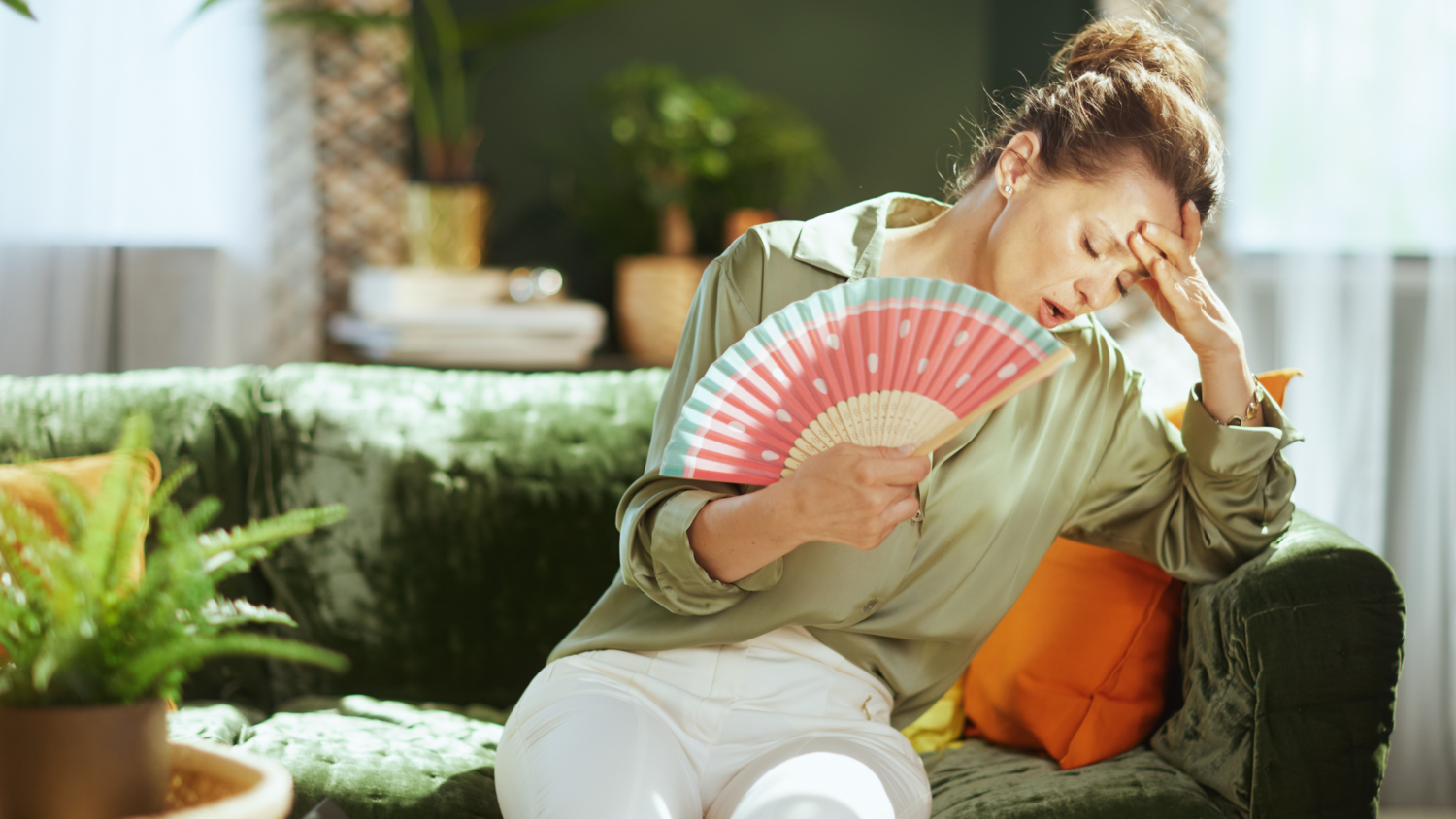 Exhausted woman using a hand fan to cool off in a humid St. Louis home, highlighting the need for a whole-house dehumidifier.